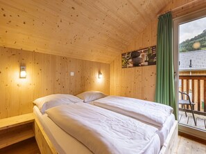 A wooden cabin room with two beds, a wooden ceiling, and a view of a balcony with a chair. - Exclusive Chalet With Whirlpool (Sankt Georgen am Kreischberg)