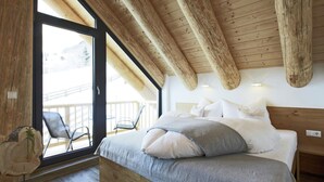 A bedroom with a large bed, wooden ceiling beams, a balcony with chairs, and a wooden floor. - Chalet in Ladis by Ski Slope & Sonnenbahn (Ladis)
