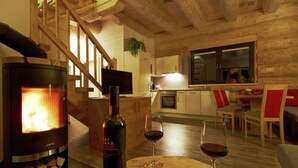 A cozy living area with a wood-burning stove, a bottle of wine, and glasses on a wooden table. A staircase leads to an upper level with a TV and kitchen area. - Chalet in Ladis by Ski Slope & Sonnenbahn (Ladis)