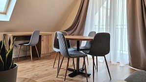 A modern dining area with a wooden table and chairs, a potted plant, and a large window with curtains. - Ornak 7 (Zakopane)