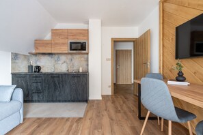 A modern kitchen with dark cabinets, a microwave, and a sink. There is a dining area with a table and chairs, and a TV mounted on the wall. - Ornak 7 (Zakopane)