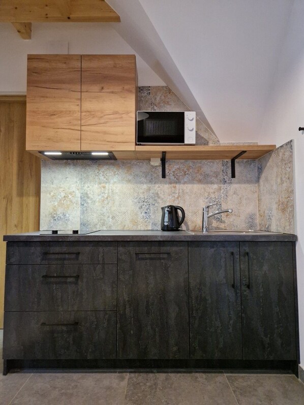 Una cocina con armarios oscuros, encimera de madera, microondas, hervidor y un lavabo.