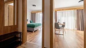 A hotel room with a wooden floor, a bed with green bedding, a desk with a chair, and a large mirror. - Ornak 7 (Zakopane)