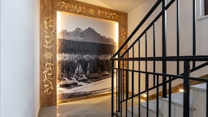 A staircase with a wooden frame and a black railing, leading to a room with a wall-mounted picture of a snowy mountain landscape. - Ornak 7 (Zakopane)