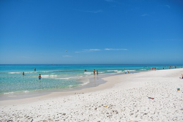 Een strand met helderblauw water, wit zand en mensen die van het strand genieten.