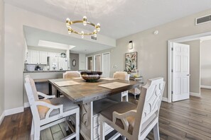 Een eetruimte met een houten tafel, witte stoelen, een decoratieve kom en een kroonluchter.