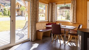 A wooden cabin with a dining area, large windows, and a view of the surrounding area.