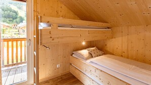 A wooden cabin room with a bunk bed, a balcony, and a view of houses in the background.