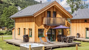 A wooden cabin with a balcony, outdoor seating, and a hot tub.