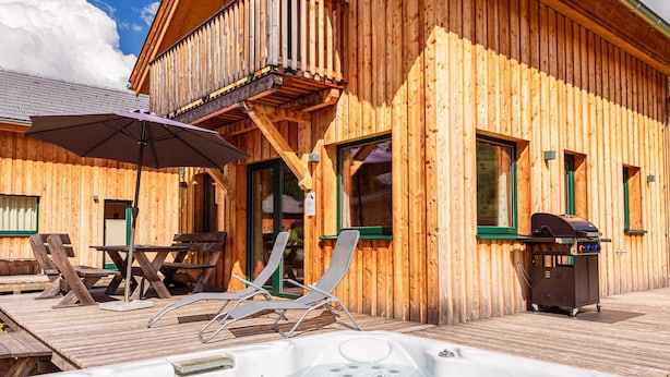 A wooden cabin with a hot tub, outdoor seating, and a barbecue grill.