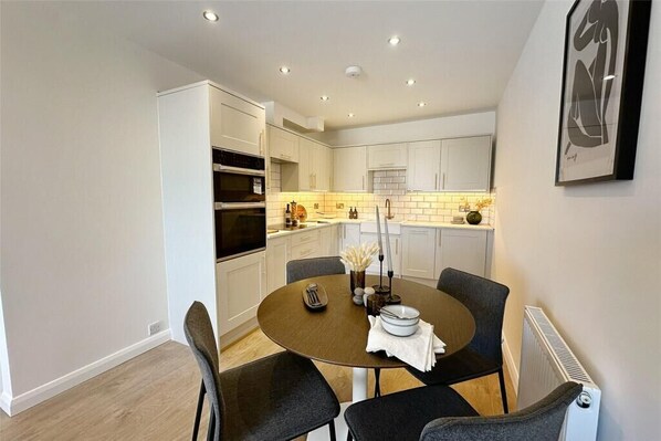 A modern kitchen with white cabinets, a round dining table with four chairs, and a built-in oven.