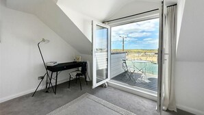 A room with a desk, chair, and a view of a pool and beach through a large sliding glass door.