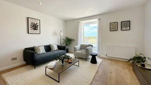 A modern living room with a sofa, armchair, coffee table, and artwork on the walls.