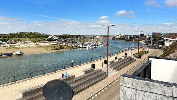 A waterfront promenade with a marina, steps leading down to the water, and a clear sky.