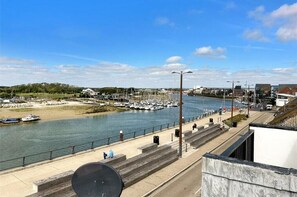 Un paseo marítimo con un puerto deportivo, escaleras que bajan al agua y un cielo despejado.