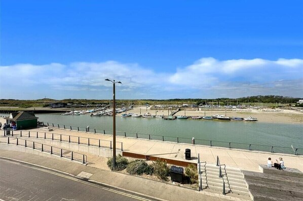 Una marina costera con barcos amarrados, un paseo peatonal y un pequeño edificio verde.