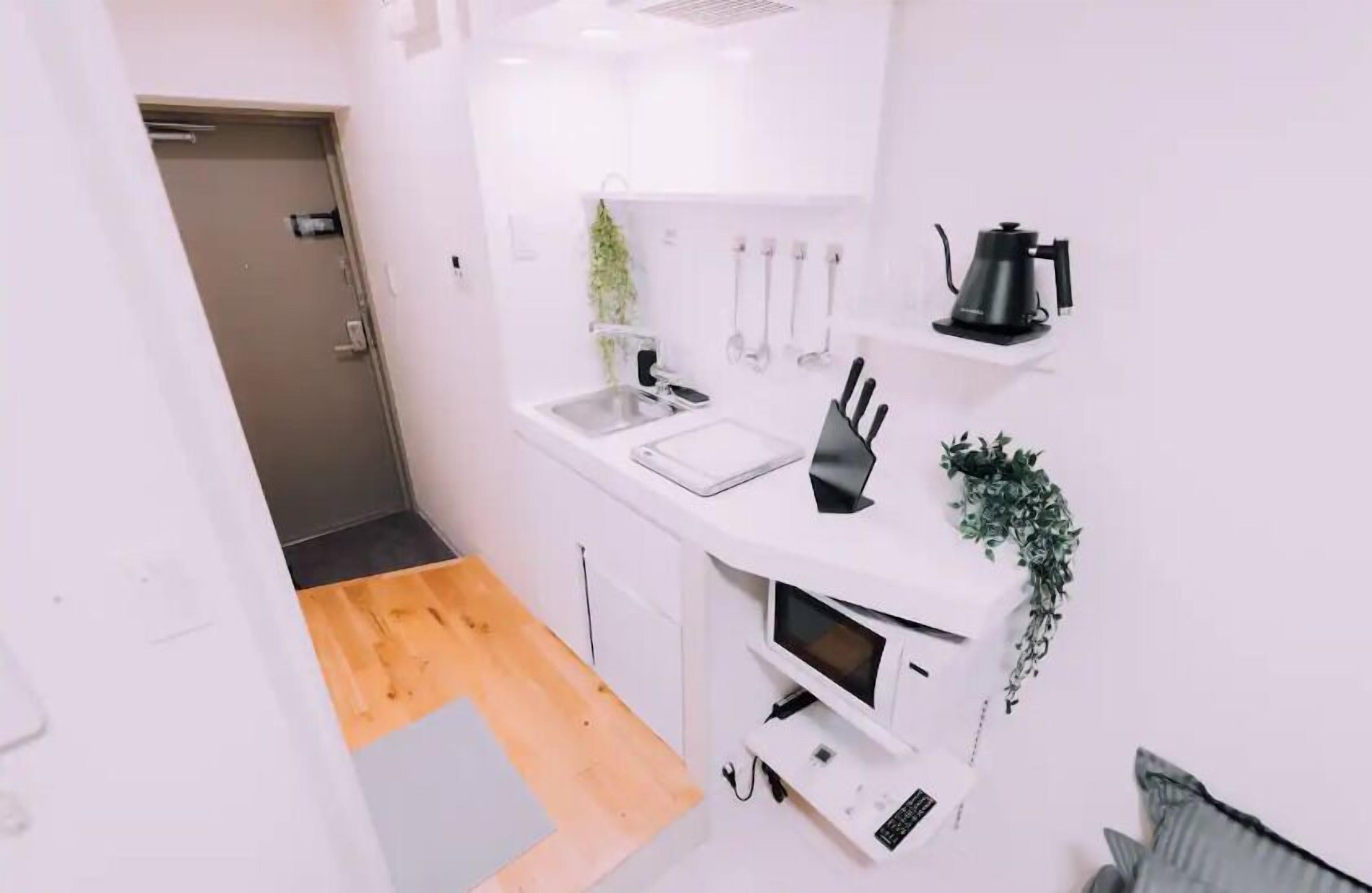 A compact kitchen with white cabinets, a sink, a microwave, and a kettle.