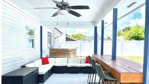 Un espace extérieur abrité, avec une table et des chaises en bois, un ventilateur de plafond et une vue sur le jardin.