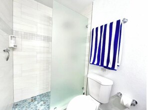 A bathroom with a shower, toilet, and a towel rack with a blue and white striped towel. - Beach House, Pool, Garage, 10 Min to Beach (Port Orange)