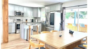Une cuisine moderne avec des meubles gris, des appareils en acier inoxydable et une table à manger en bois, assortie de chaises.