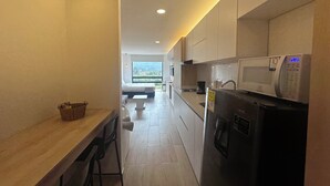 A modern kitchen with a built-in microwave, a coffee maker, and a refrigerator. There is a wooden table and chairs along the left side.