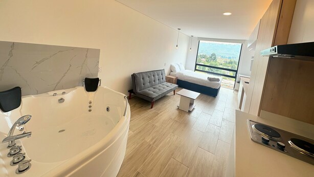 A modern bathroom with a large bathtub, a sofa, and a view of a cityscape through large windows.