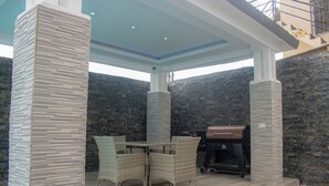 An outdoor patio with a stone wall, a grill, wicker furniture, and a pool. - Charming 3-bedroom house with AC, WiFi in delightful Bocachica (Bocachica)