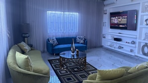 A modern living room with a blue sofa, two armchairs, a coffee table, and a TV mounted on the wall. - Charming 3-bedroom house with AC, WiFi in delightful Bocachica (Bocachica)