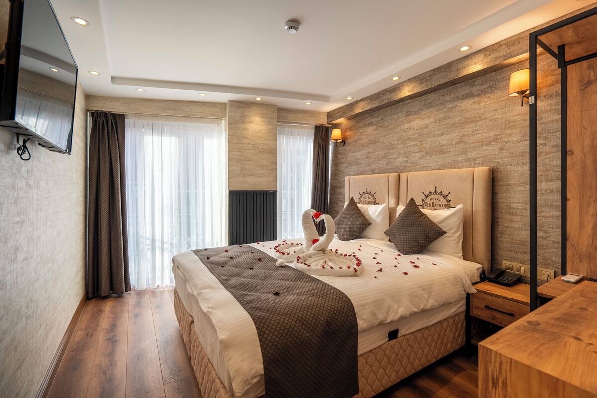 A hotel room with a large bed, a flat-screen TV mounted on the wall, a wooden nightstand, and a wooden desk.