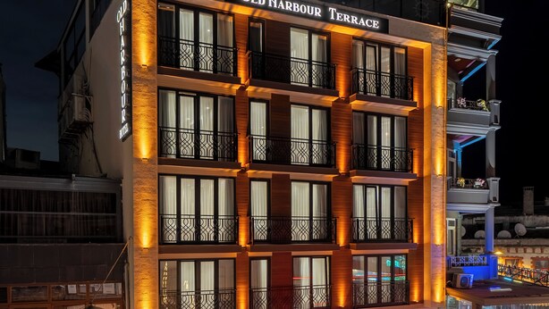 Un hotel de varios pisos con una terraza llamada 'Old Harbour Terrace'. Presenta un diseño arquitectónico moderno con balcones y grandes ventanales.