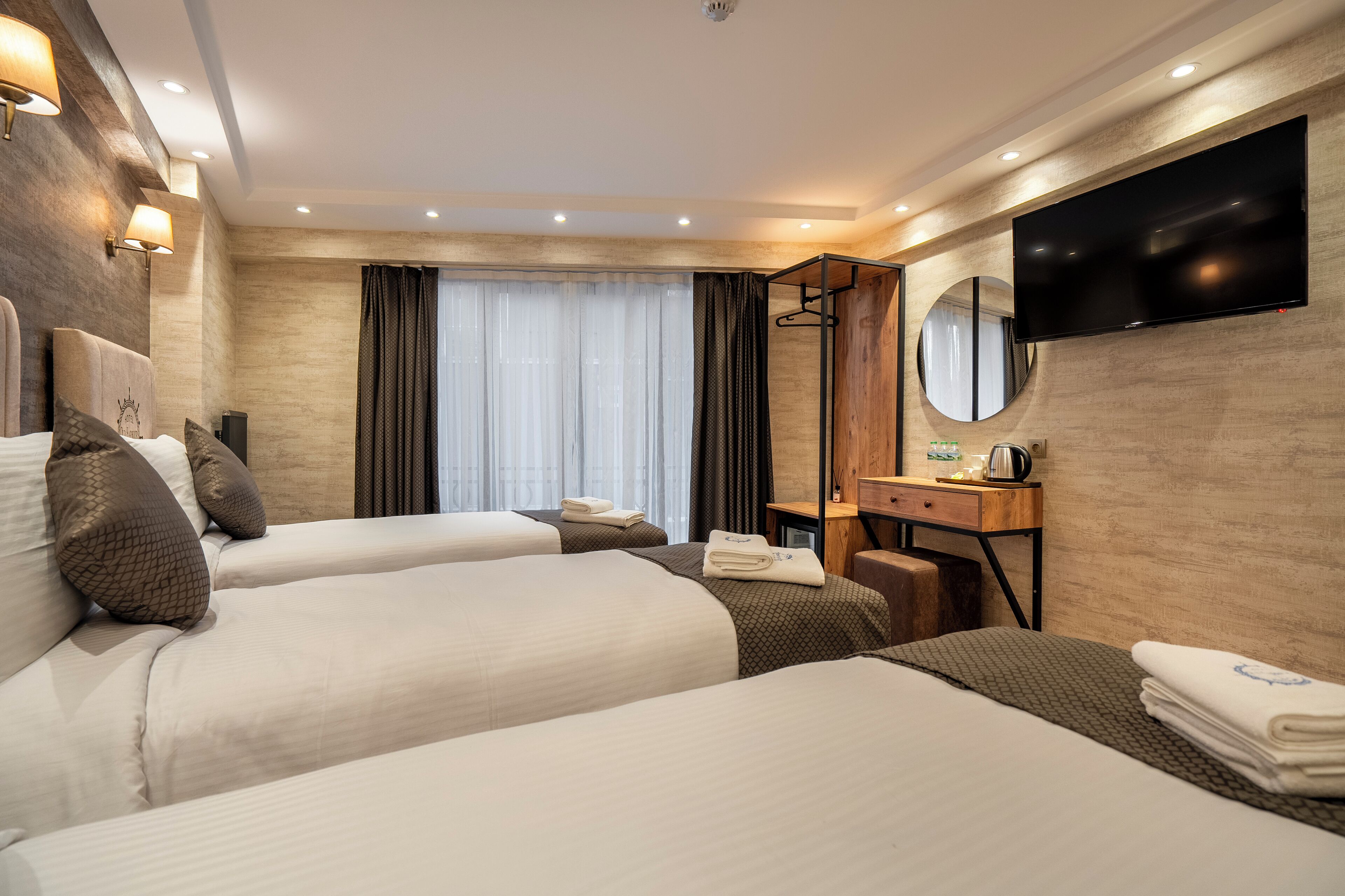 Une chambre d’hôtel avec deux lits, une télévision, un miroir, un bureau et une fenêtre avec des rideaux.