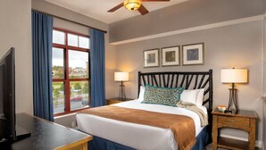Une chambre d’hôtel avec un lit, deux lampes de chevet, un ventilateur de plafond, une télévision et une fenêtre avec des rideaux.