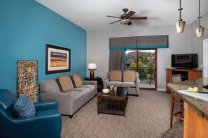A living room with a blue wall, two sofas, a coffee table, a TV, and a balcony with a view.