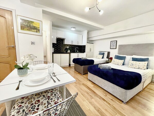 A modern apartment with a dining area, kitchenette, and a bedroom with two beds.