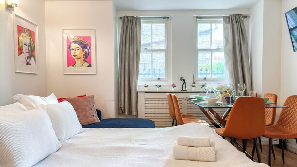 Una habitación de hotel con una cama, una mesa de comedor con sillas y dos ventanas con cortinas.