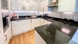 Una cocina moderna con armarios blancos, encimera negra y campana extractora de acero inoxidable.