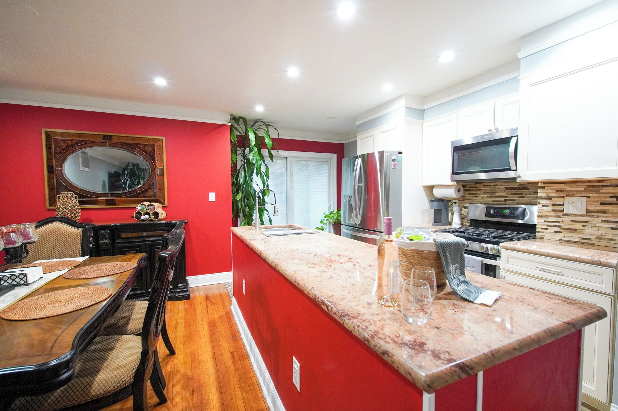 A modern kitchen with a red accent wall, a dining area with a wooden table and chairs, and a large island with a sink.