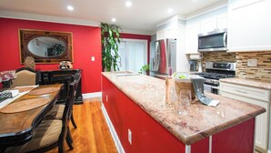 Una cocina moderna con una pared de acento roja, un comedor con mesa y sillas de madera, y una isla grande con pileta.