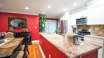 A modern kitchen with a red accent wall, a dining area with a wooden table and chairs, and a large island with a sink.