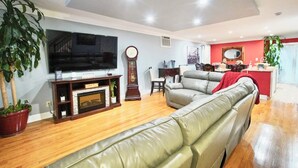 Una sala de estar con una televisión de pantalla plana grande, chimenea, sofá y comedor con pared roja y espejo.