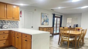 A modern kitchen with wooden cabinets, a white countertop, and a dining area with a wooden table and chairs. - POOL House+Garage. Bring your Bikes! + 3Bed/2Bath
 (Port Orange)