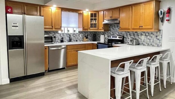 A modern kitchen with wooden cabinets, stainless steel appliances, and a central island with bar stools. - POOL House+Garage. Bring your Bikes! + 3Bed/2Bath
 (Port Orange)