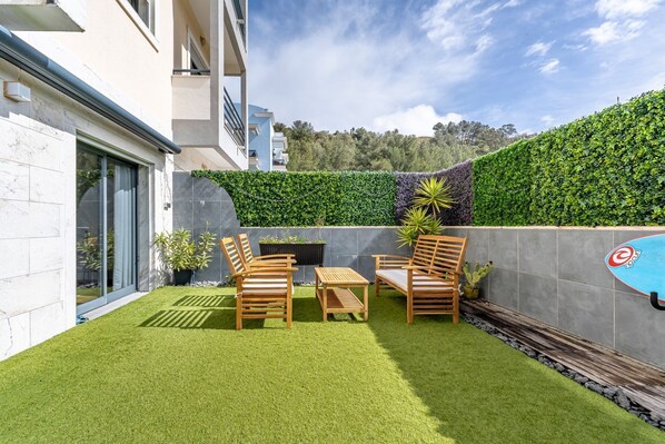 A modern outdoor patio with artificial grass, wooden furniture, and a variety of plants. - Cozy apartment in charming Costa da Caparica with AC, WiFi (Costa da Caparica)