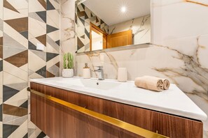 A bathroom with a marble sink, wooden vanity, and a geometric patterned wall. - Cozy apartment in charming Costa da Caparica with AC, WiFi (Costa da Caparica)
