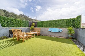 A patio area with a pool, wooden furniture, and a green hedge wall. - Cozy apartment in charming Costa da Caparica with AC, WiFi (Costa da Caparica)