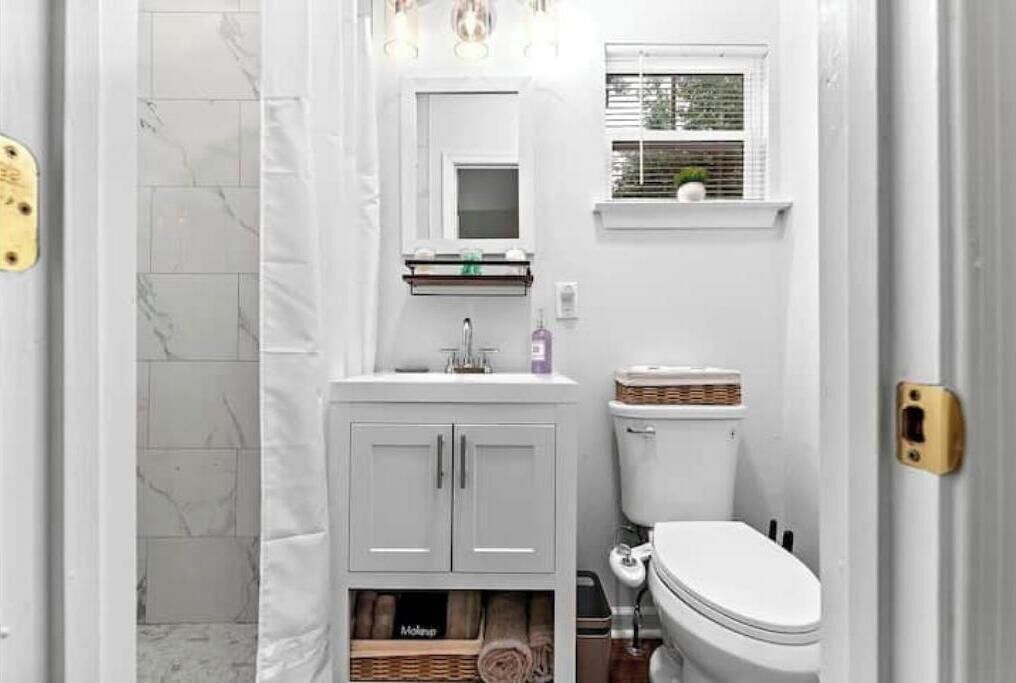 A bathroom with a toilet, sink, and mirror. There is a window above the sink and a towel rack below the mirror.