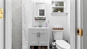 A bathroom with a toilet, sink, and mirror. There is a window above the sink and a towel rack below the mirror.