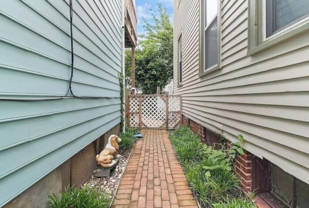 A narrow brick pathway between two houses with a white fence and a dog statue.