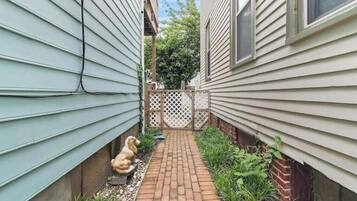 A narrow brick pathway between two houses with a white fence and a dog statue.
