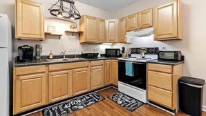 Una cocina con armarios de madera, estufa, microondas y un cubo de basura.